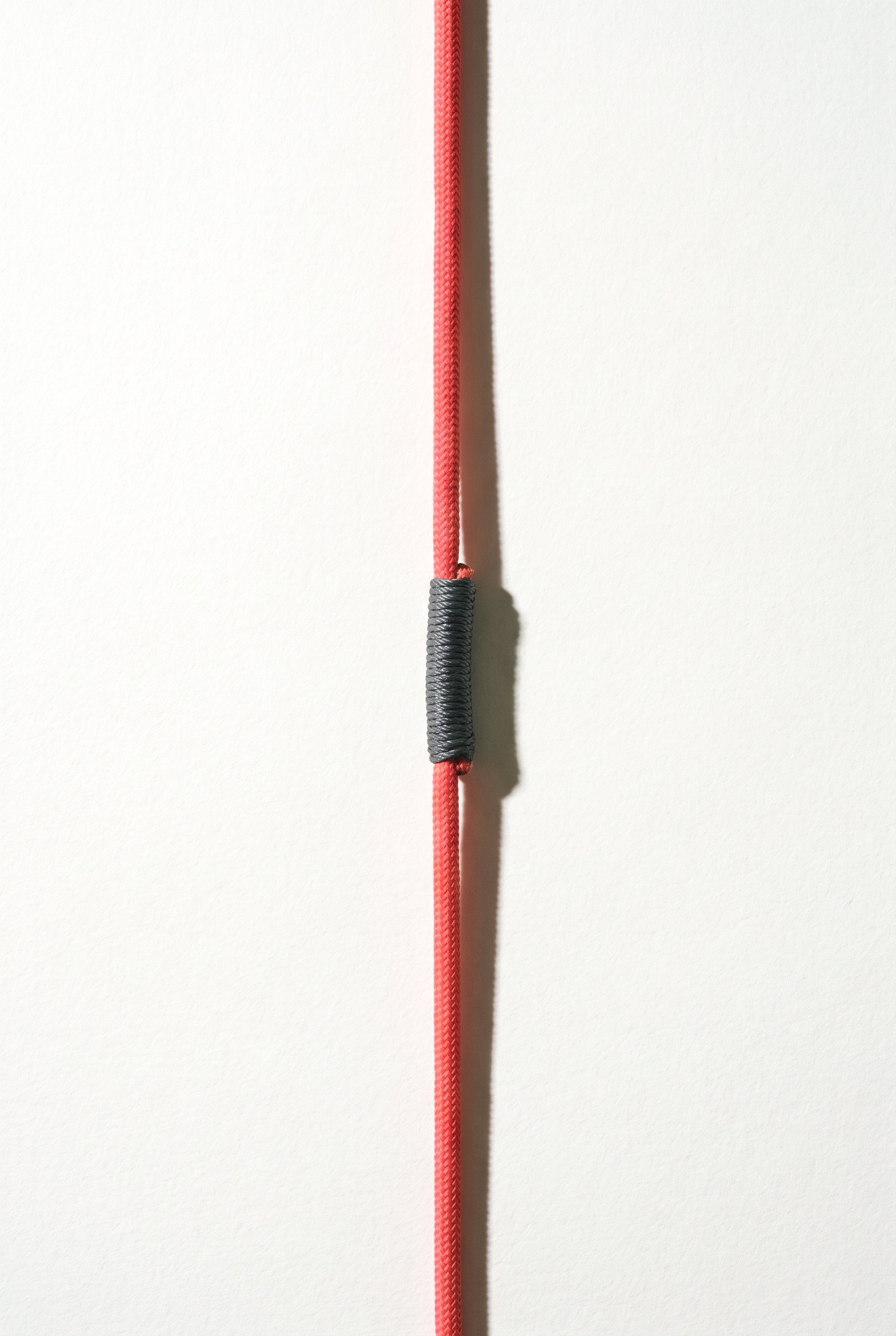 A single taut coral cord running vertically, joined back together at one point by a neat graphite whipping, with the tension restored through the join.