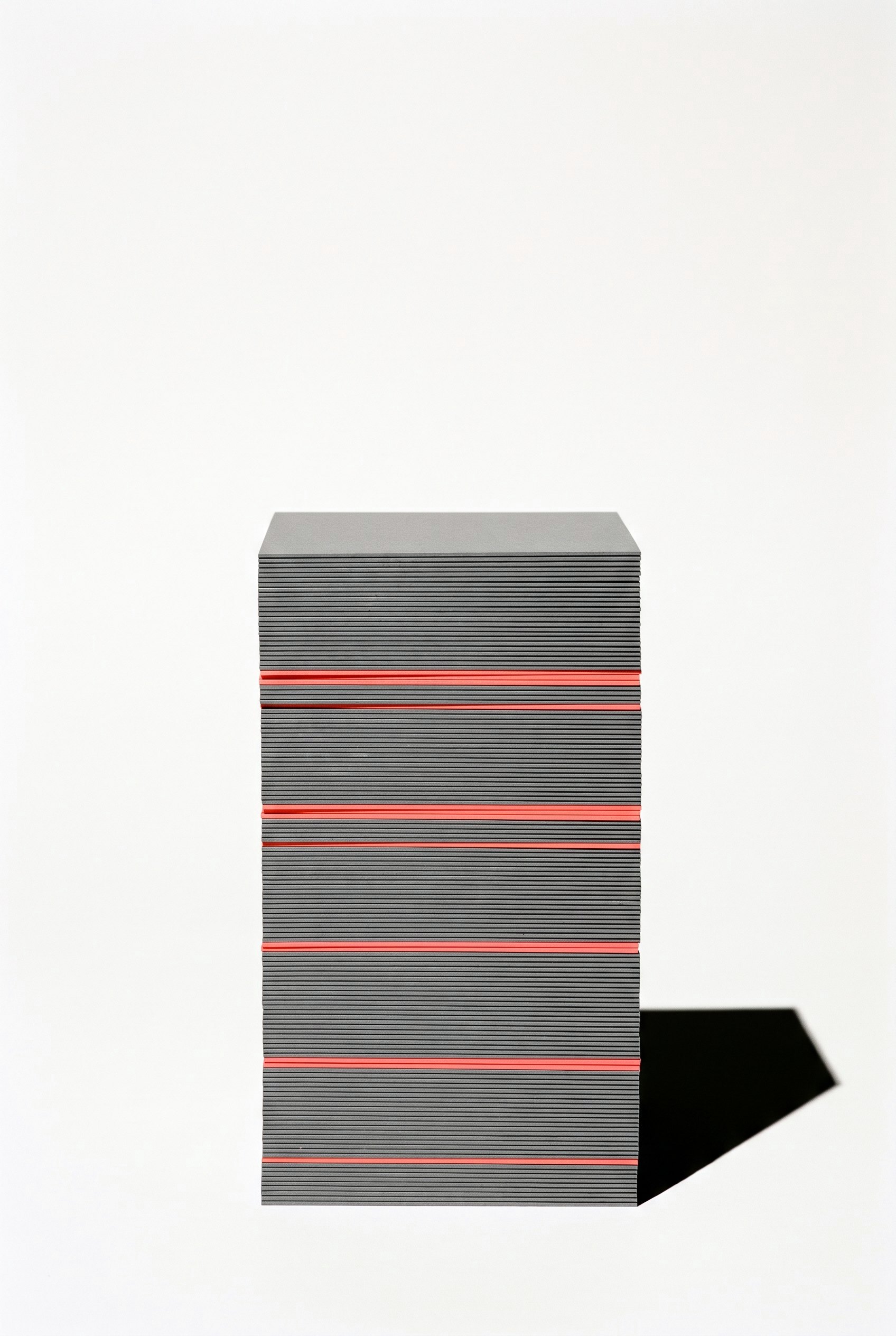 A tall stack of many thin grey cards seen edge-on, with a few coral cards set through it so their edges read as bright lines among the layers.